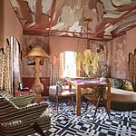 Eclectic room with patterned walls, unique chandelier, colorful furniture, and geometric black-and-white floor design.