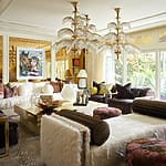 Luxurious living room with eclectic decor, colorful artwork, plush seating, unique chandelier, and large windows overlooking a garden.