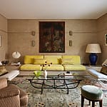 Elegant living room with yellow sofa, glass coffee table, and decorative rug, featuring wall art and stylish lighting.