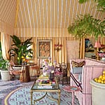 Vibrant living room with striped yellow and pink decor, plants, and colorful furniture under a canopy ceiling.