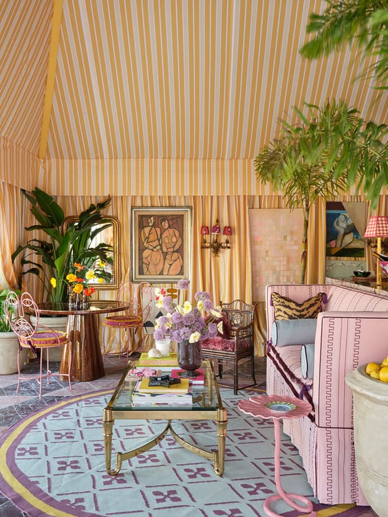 Vibrant living room with striped yellow and pink decor, plants, and colorful furniture under a canopy ceiling.