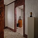 Artistic hallway with sculpted white walls, decorative paneling, and sculptures on pedestals leading to a room.