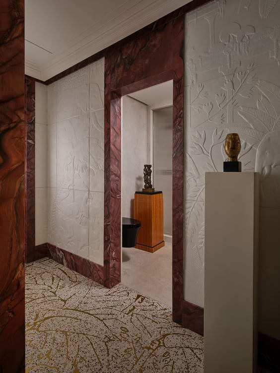 Artistic hallway with sculpted white walls, decorative paneling, and sculptures on pedestals leading to a room.