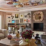 Stylish living room with eclectic art, modern furniture, floral arrangement on a table, and unique ceiling decor elements.