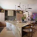 Modern kitchen with large marble island, wooden cabinets, stylish pendant lights, and decorative wall art.