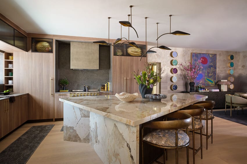 Modern kitchen with large marble island, wooden cabinets, stylish pendant lights, and decorative wall art.