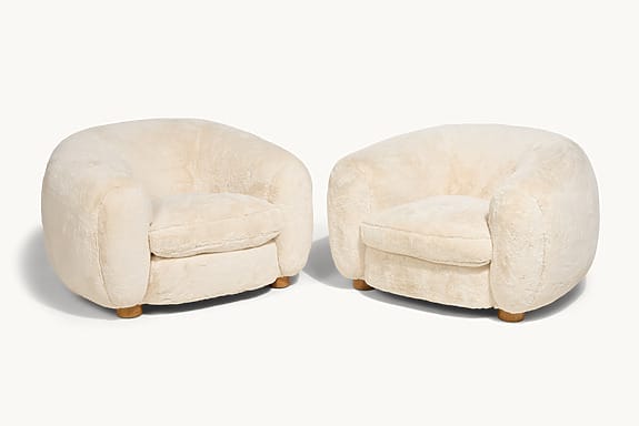 Two plush, cream-colored, round armchairs with wooden legs on a white background.