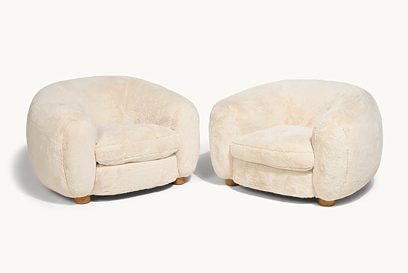 Two plush, cream-colored, round armchairs with wooden legs on a white background.