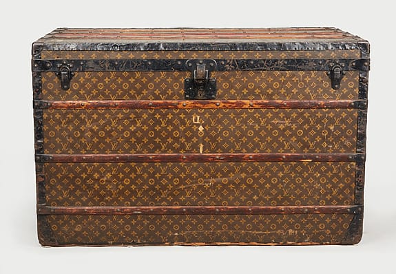 Vintage travel trunk with monogram pattern, metal clasps, and wooden slats, showcasing classic design and craftsmanship.
