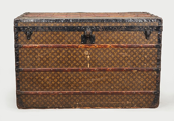 Vintage travel trunk with monogram pattern, metal clasps, and wooden slats, showcasing classic design and craftsmanship.