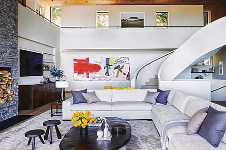 Modern living room with large sectional sofa, abstract art on walls, and spiral staircase in a bright, open space.