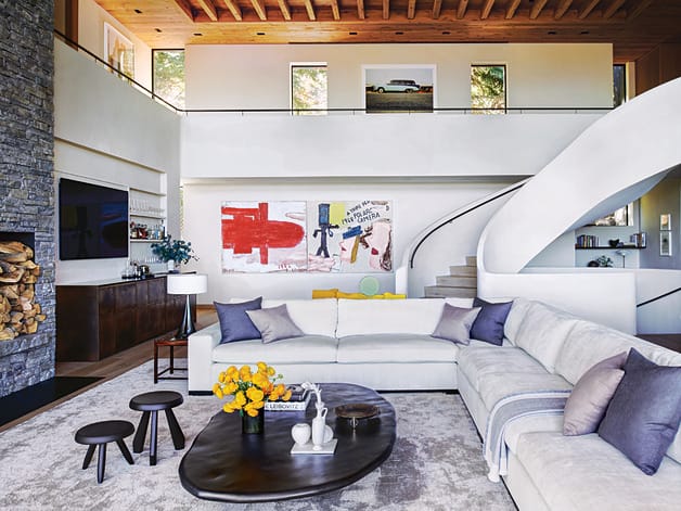 Modern living room with large sectional sofa, abstract art on walls, and spiral staircase in a bright, open space.