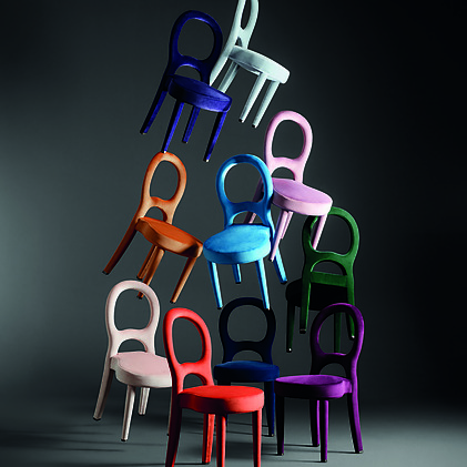 A stack of colorful, modern chairs in various shades against a dark background, showcasing unique design and vibrant hues.