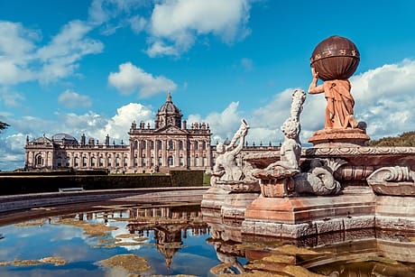 Statues and a reflecting pool in front of a large historic building under a blue sky with scattered clouds