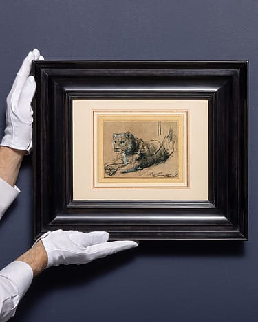 Hands in gloves holding a framed sketch of a lion on a navy blue wall background.