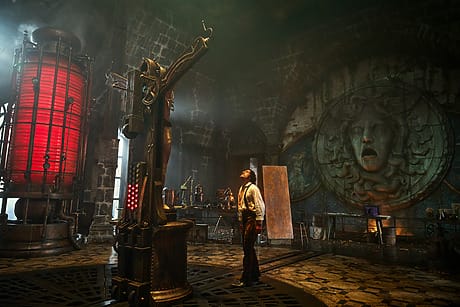 A person stands in a gothic, steampunk room with a large red cylinder and Medusa face on the wall.
