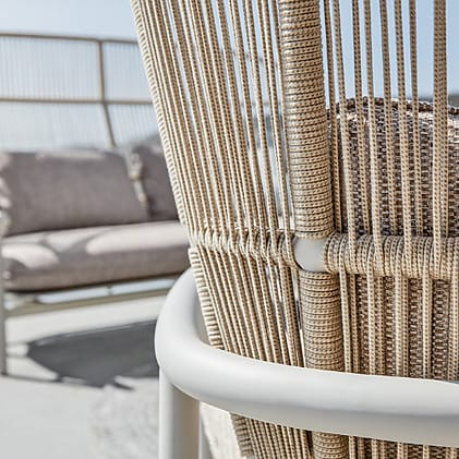 Close-up of modern outdoor wicker furniture with beige cushions in a minimalist patio setting.