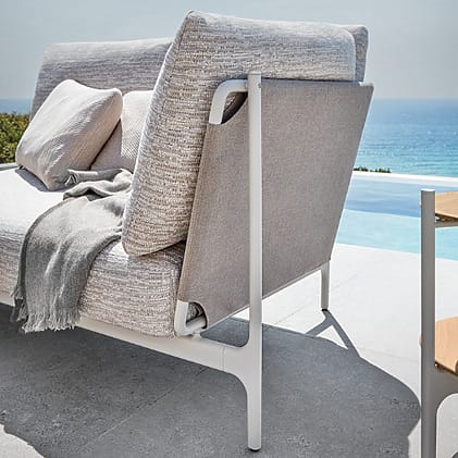 Outdoor sofa with cushions on a patio overlooking a pool and ocean.