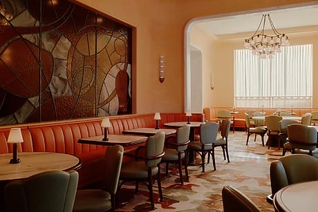 Cozy retro-style restaurant interior with stained glass wall, vintage lighting, and pastel-colored seating arrangement.
