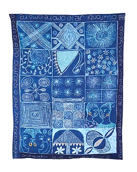 Blue textile art with geometric patterns and faces, featuring symbols like stars and a teapot, surrounded by text in a script.