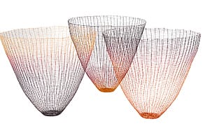 Three colorful, wire mesh baskets with gradient hues of black, orange, and red, artistically arranged on a white background.
