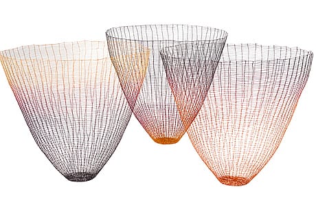Three colorful, wire mesh baskets with gradient hues of black, orange, and red, artistically arranged on a white background.