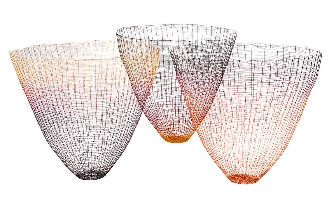 Three colorful, wire mesh baskets with gradient hues of black, orange, and red, artistically arranged on a white background.