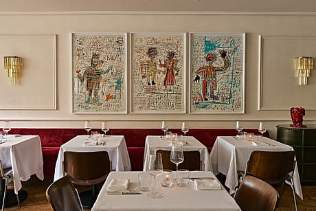 Contemporary restaurant interior with white tablecloths, wooden chairs, and abstract art on the wall.