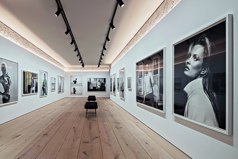 Modern art gallery with framed black and white photographs on white walls, wooden floor, and track lighting overhead.