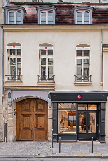 Street view of a historic European building with large wooden doors and a modern store entrance on the right.