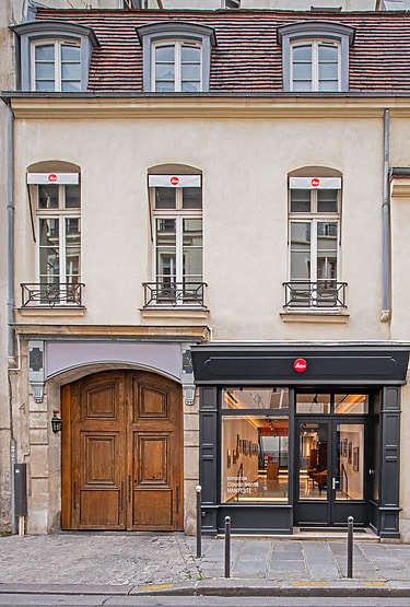 Street view of a historic European building with large wooden doors and a modern store entrance on the right.