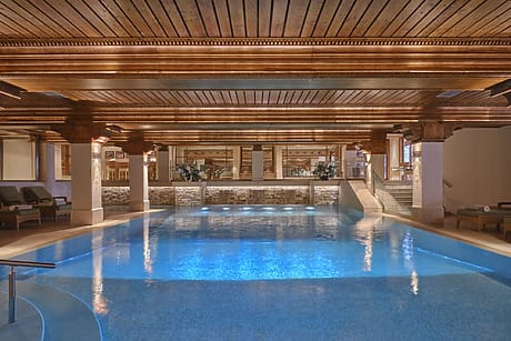 Luxurious indoor pool with wooden ceiling, ambient lighting, and several loungers around the pool area.
