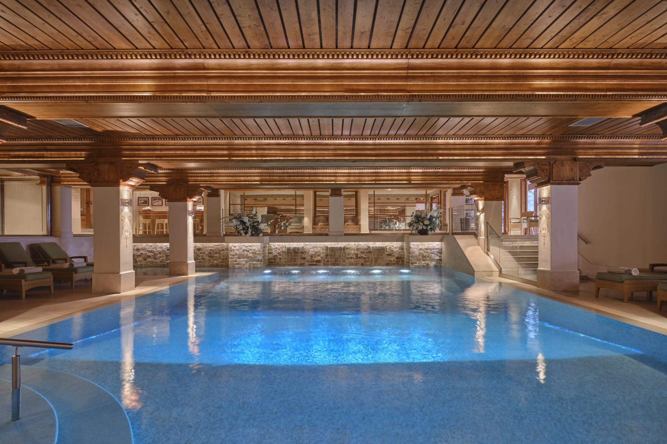 Luxurious indoor pool with wooden ceiling, ambient lighting, and several loungers around the pool area.