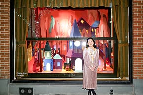 Storefront with a vibrant, colorful display and a person standing in front, showcasing festive decorations and small houses.