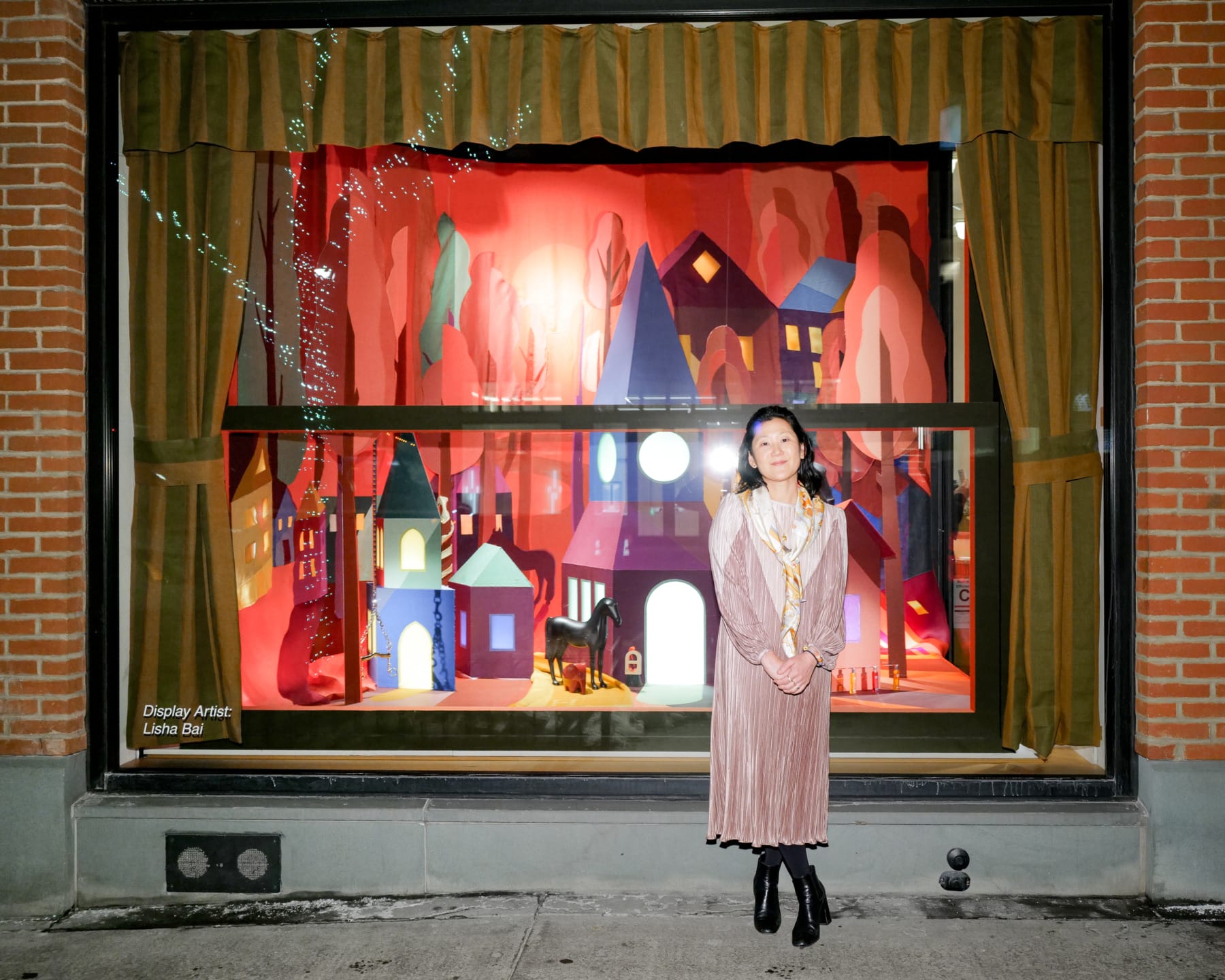 Storefront with a vibrant, colorful display and a person standing in front, showcasing festive decorations and small houses.