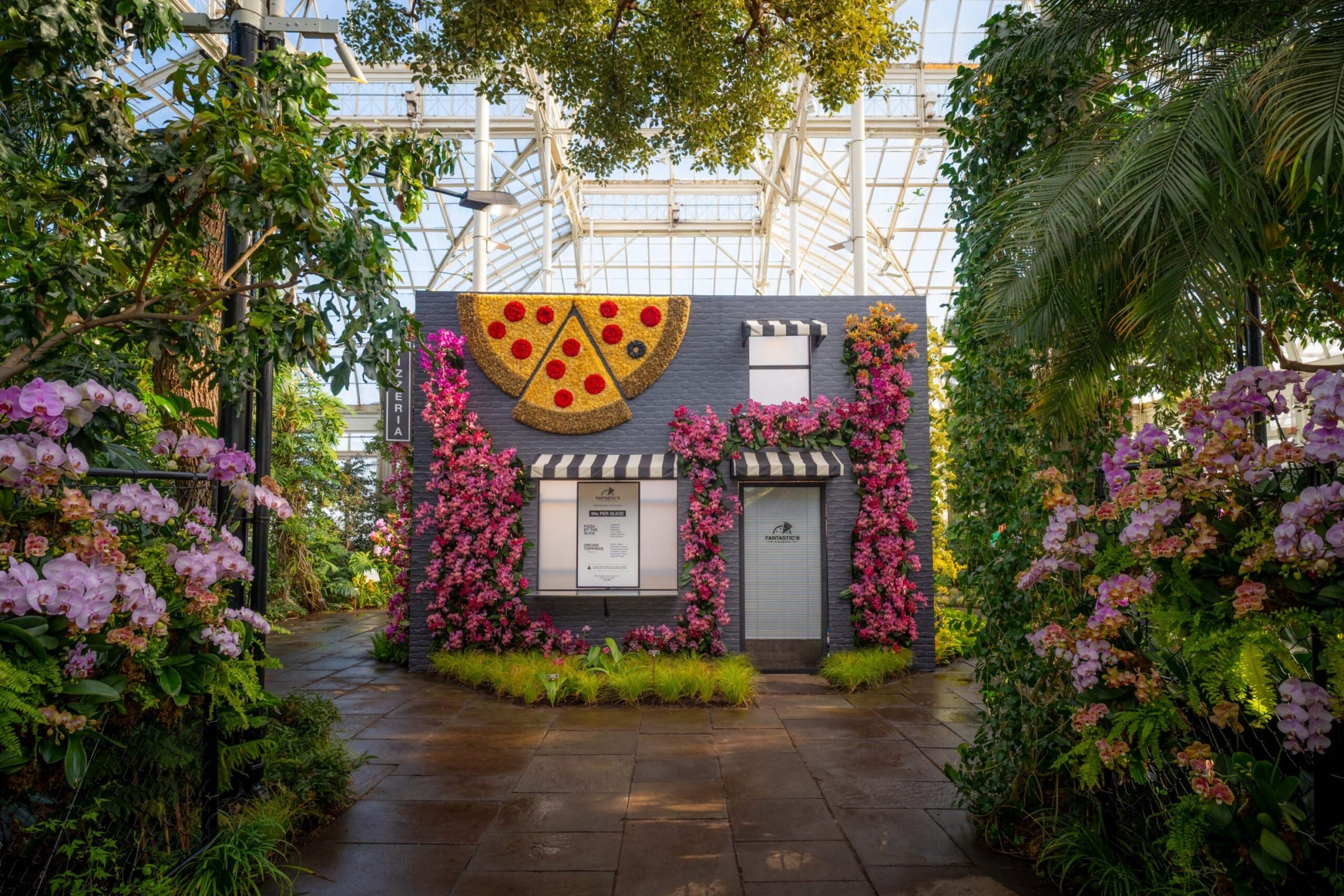 Botanical garden with a small brick building adorned with floral displays and a large pizza slice decor.