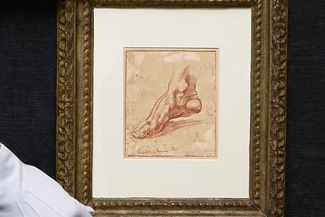 Gloved hands holding a framed sketch of a foot on a dark fabric background
