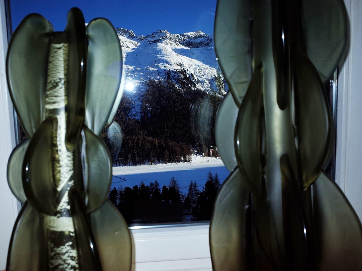 View through decorative window with greenish abstract glass, showing snowy mountains and trees in the distance.