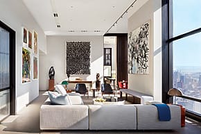 Modern living room with large windows, abstract art on walls, white sectional sofa, and city skyline view.
