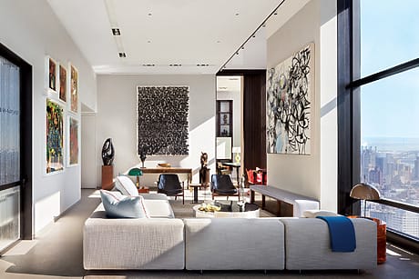 Modern living room with large windows, abstract art on walls, white sectional sofa, and city skyline view.