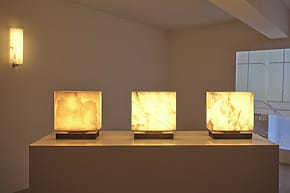 Three illuminated cube lamps on a pedestal in a dimly lit room with minimalistic decor.