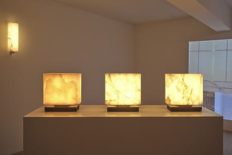Three illuminated cube lamps on a pedestal in a dimly lit room with minimalistic decor.