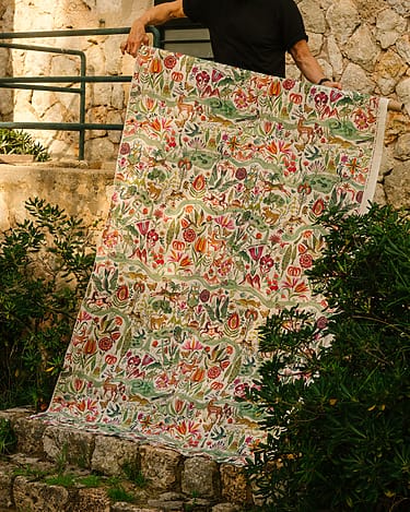 Person holding large floral fabric with colorful patterns in an outdoor garden setting.