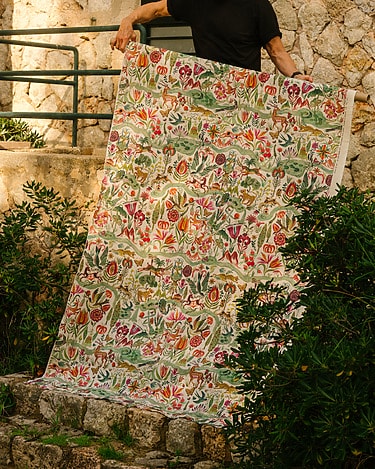 Person holding large floral fabric with colorful patterns in an outdoor garden setting.