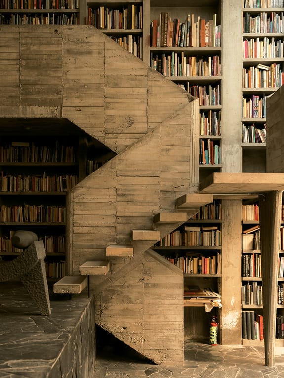 Concrete staircase in a modern library with shelves full of books and a cozy reading nook underneath.