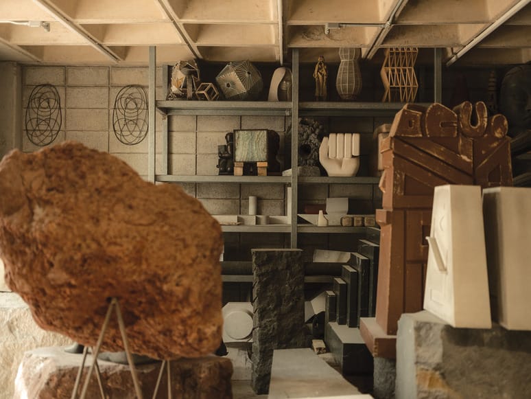 Artistic sculptures and geometric shapes displayed on shelves and stands in a studio with concrete walls and ceiling.