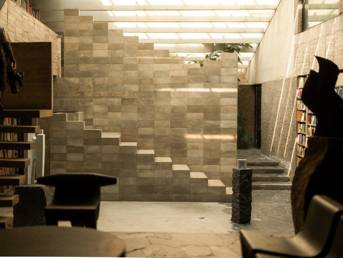 modern interior with geometric staircase stone wall natural light and shelves filled with books art pieces in the foreground