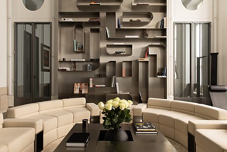 Modern living room with curved beige sofas, dark coffee table, and artistic wall shelves filled with books and decor items.
