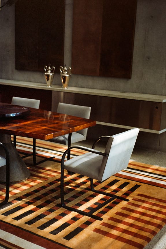 Modern dining room with a wooden table, upholstered chairs, and a geometric patterned rug.