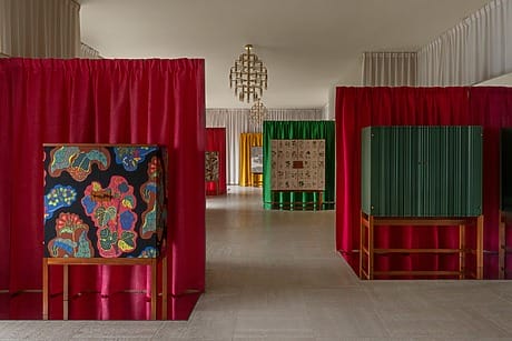 Art exhibition with colorful cabinets and vibrant curtains in a spacious room with chandeliers in the background.